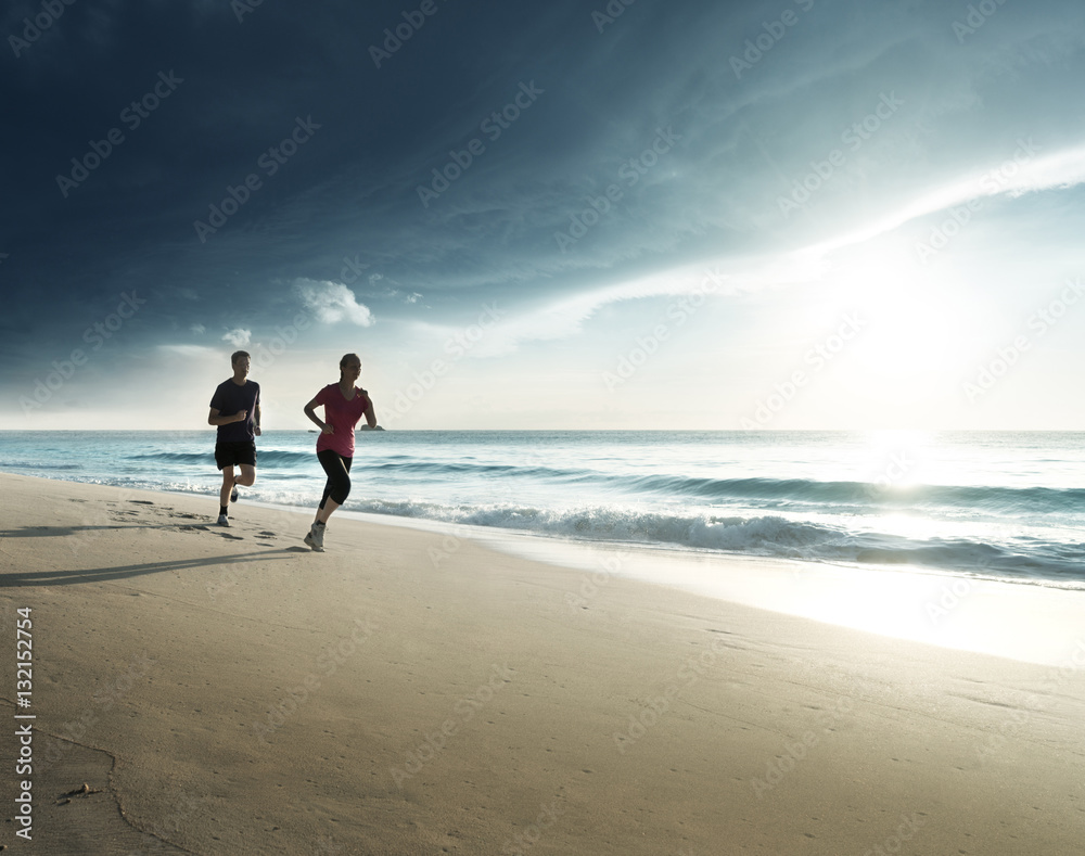 Naklejka premium Man and women running on tropical beach at sunset