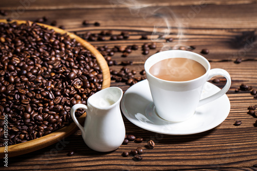 Coffee on a large plate and a cup of fragrant hot coffee with milk on a wooden table.