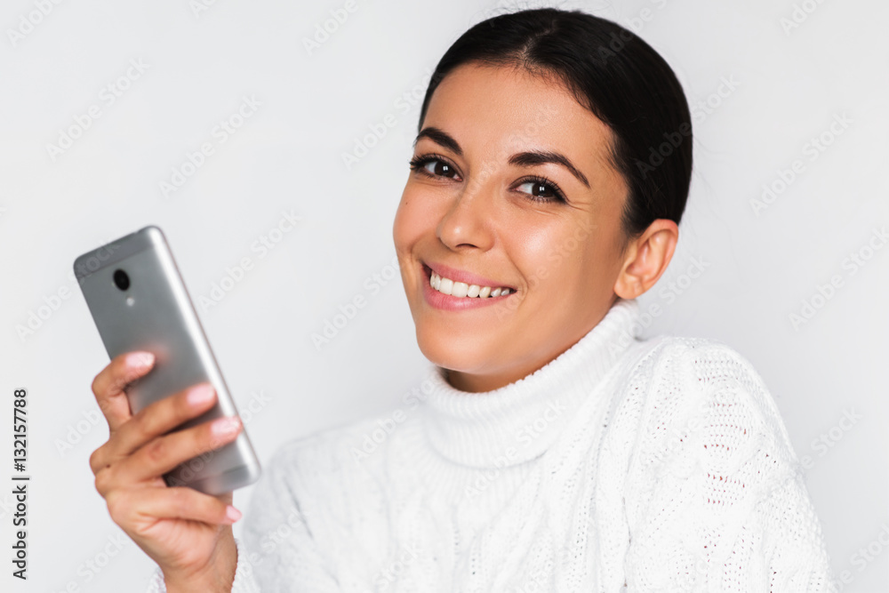 Portrait of attractive young happy woman with mobile phone with pretty toothy smile, on the white background. Brunette beautiful cheerful woman using smart phone in hand.