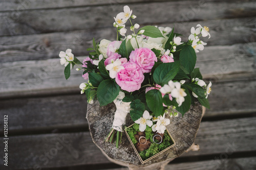 Fototapeta Naklejka Na Ścianę i Meble -  Beautiful bouquet of jasmine and pink garden roses and a box with moss and wedding rings on old wooden stump