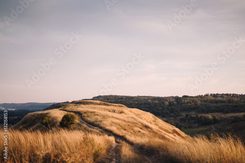 Fototapeta Naklejka Na Ścianę i Meble -  Evening walk outside the city. Beautiful hill covered with dry grass at sunset, colorful pastel sky.