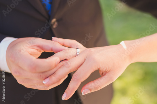 Closeup of a groom putting a gold wedding ring onto the bride's finger © anna_gorbenko
