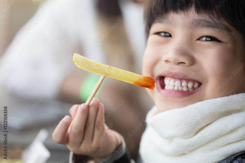 Beautiful laughing little girl sitting at table and eating French fries