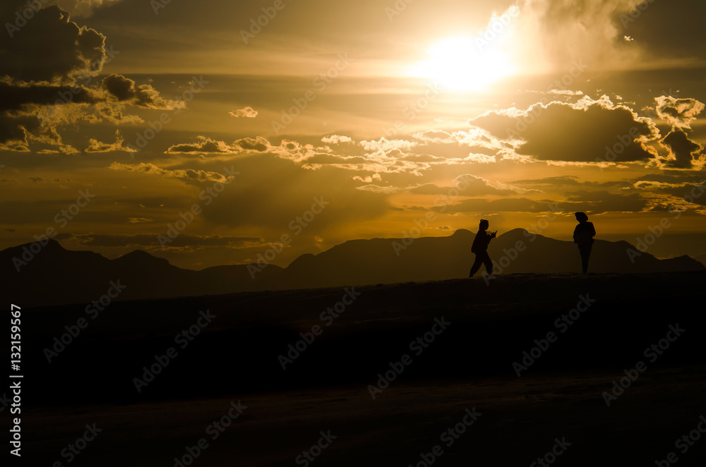 Silhouettes of two people walking on White Sand Dunes during sun Silhouettes of two people walking on White Sand Dunes during sun