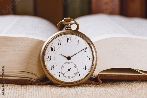 Vintage pocket clock on book against books background