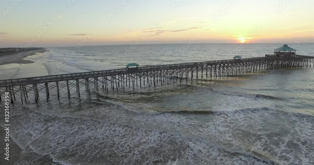 Aerial shot of the Folly Beach fishing pier at sunrise with gentle waves from the Atlantic Ocean. Aerial shot of the Folly Beach fishing pier at sunrise with gentle waves from the Atlantic Ocean.