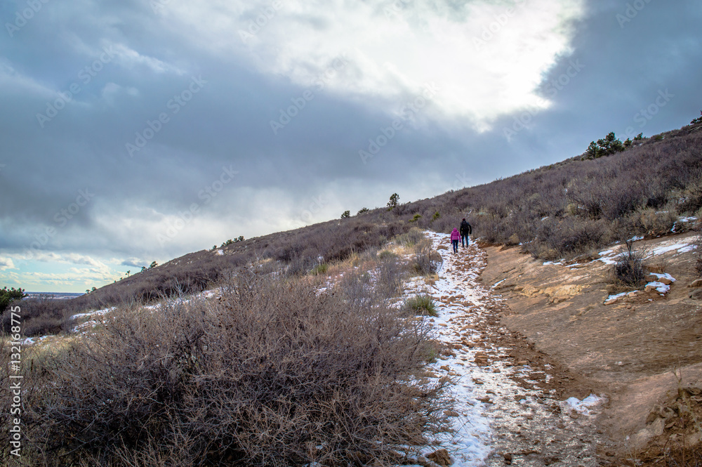 Fototapeta premium Hikers on a snowy Colorado mountain trail in brush landsape.