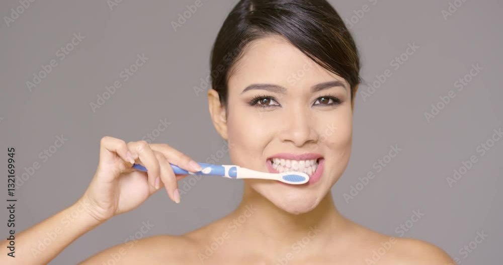 Sensual young woman cleaning her teeth with a toothbrush running her tongue over her teeth cropped head shot on grey Sensual young woman cleaning her teeth with a toothbrush running her tongue over her teeth cropped head shot on grey