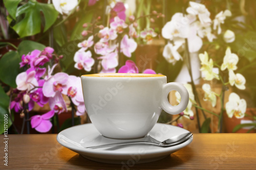 Cup of aromatic coffee on table against blurred floral background. Flower bar concept