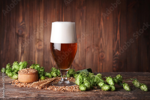 Glass of dark beer and its ingredients on table against blurred wooden background