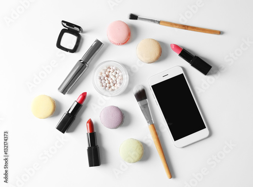 Makeup cosmetic with macaroons and phone on white background