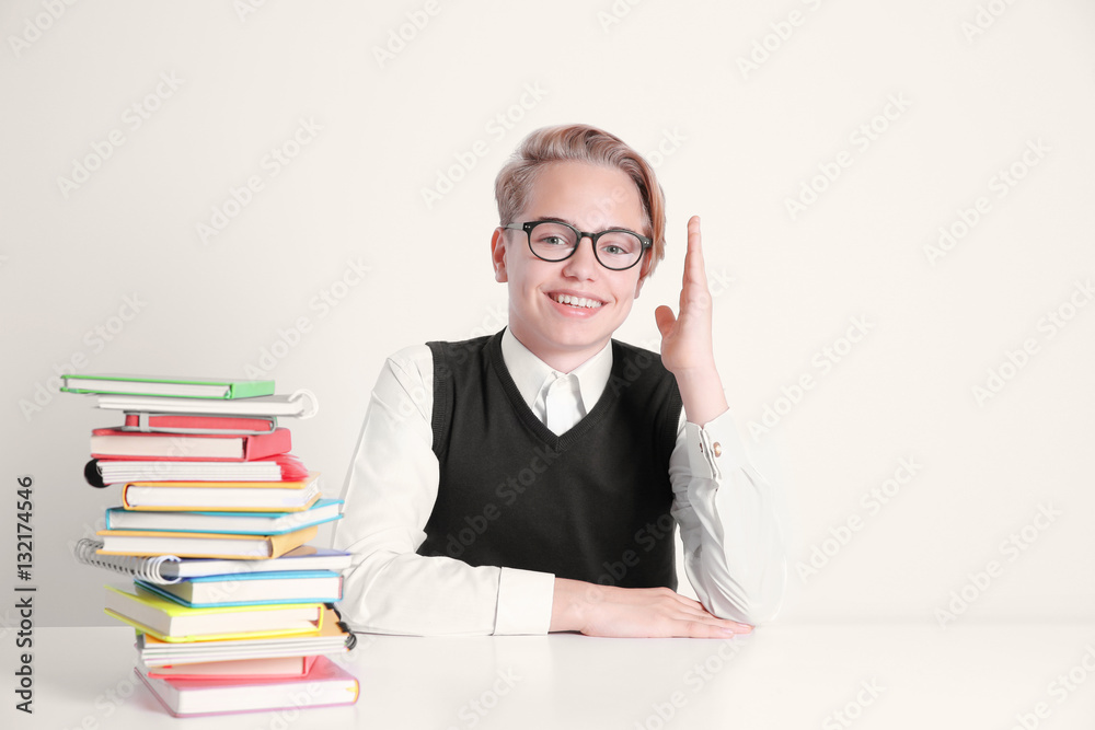 Pupil with pile of books sitting at table on white background