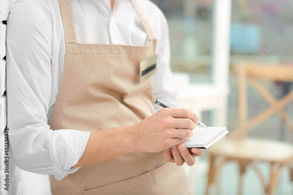 Waiter in beige apron writing down an order in a cafe, close up