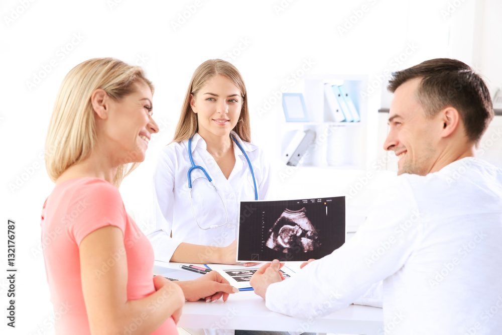Gynecology consultation. Doctor showing ultrasound scan of baby to couple Gynecology consultation. Doctor showing ultrasound scan of baby to couple