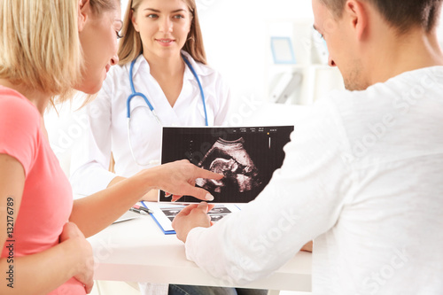 Gynecology consultation. Doctor showing ultrasound scan of baby to couple