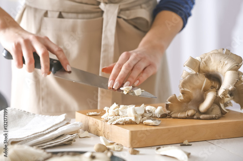 Woman cutting mushrooms on wooden board at kitchen, closeup