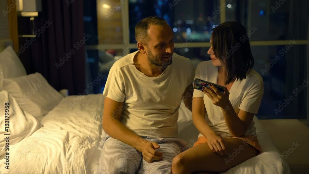 Young couple talking and browsing web on smartphone in bedroom at night
Young couple talking and browsing web on smartphone in bedroom at night