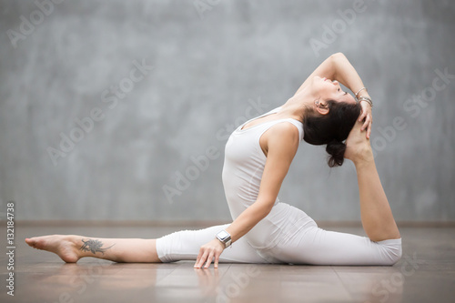 Photography Young pretty woman wearing white sportswear set and smartwatch working out against grey wall, doing yoga or pilates exercise