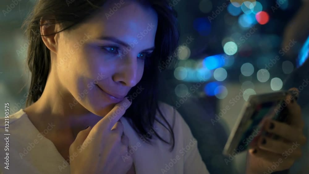 Happy, young woman watching movie on smartphone by window at night
Happy, young woman watching movie on smartphone by window at night