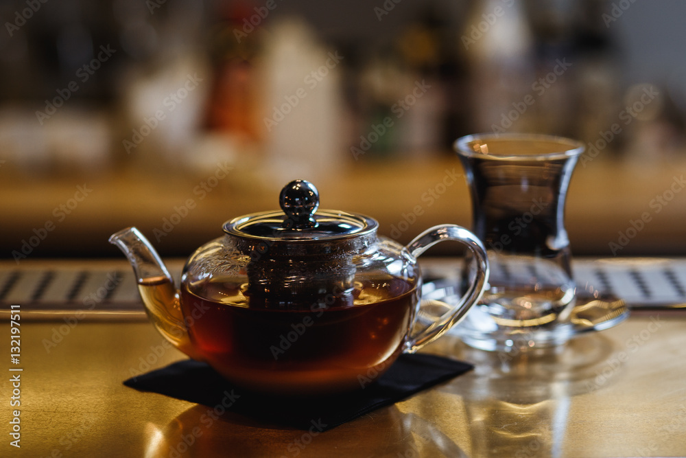 An underexposed lifestyle horizontal image of a teapot with hot alcoholic cocktail on a black tea basis. Wooden bar stand of a restaurant. An underexposed lifestyle horizontal image of a teapot with hot alcoholic cocktail on a black tea basis. Wooden bar stand of a restaurant.