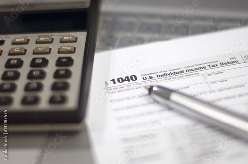 Tax Season: 1040 U.S. Individual Income Tax Return Form horizontal top view with an office laptop and blue calculator as background together with a red white pen preparation on taxation as foreground