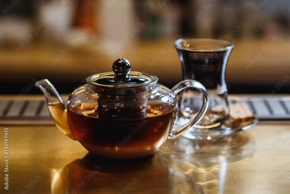 An underexposed lifestyle horizontal image of a teapot with hot alcoholic cocktail on a black tea basis. Wooden bar stand of a restaurant. An underexposed lifestyle horizontal image of a teapot with hot alcoholic cocktail on a black tea basis. Wooden bar stand of a restaurant.