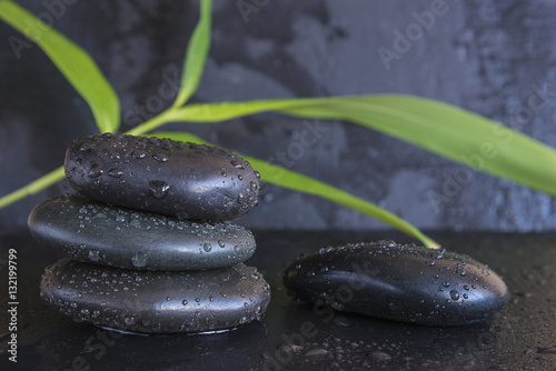 spa concept/black massage stones and bamboo leaves on black slate background with water drops