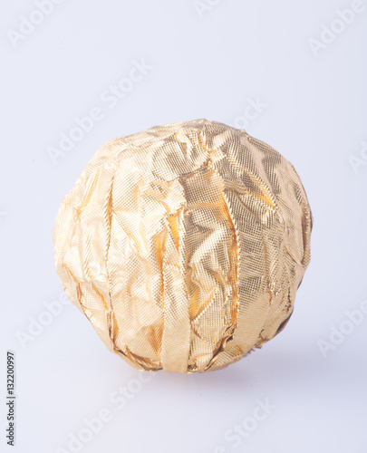 Chocolate ball in a gold foil paper on a background.