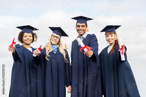 happy students in mortar boards with diplomas