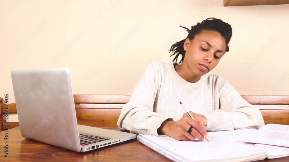 Beautiful mixed race woman studying or working at home. Black girl with dreadlocks alone with a computer on the table. Beautiful mixed race woman studying or working at home. Black girl with dreadlocks alone with a computer on the table.