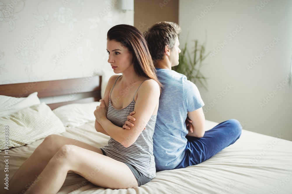Obraz premium Couple ignoring each other sitting back to back on bed