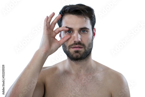 Shirtless man opening his eye with fingers