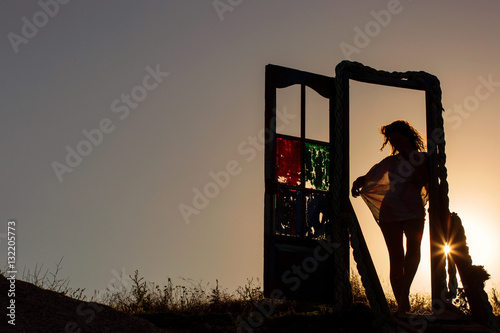 Outlines of a beautiful young woman standing by a door outside.