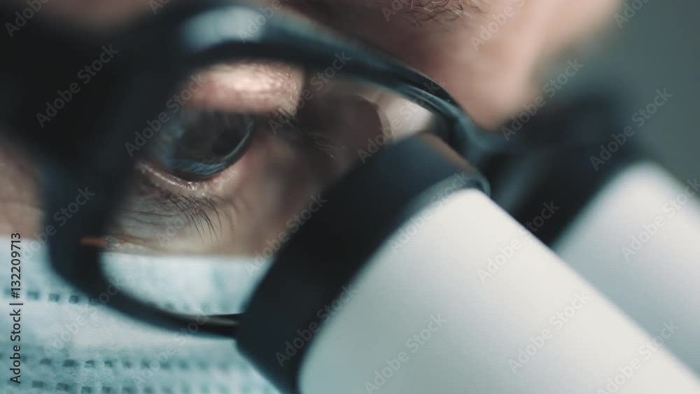 Middle age female scientist in uniform and medical face mask doing microscopic examination in laboratory.