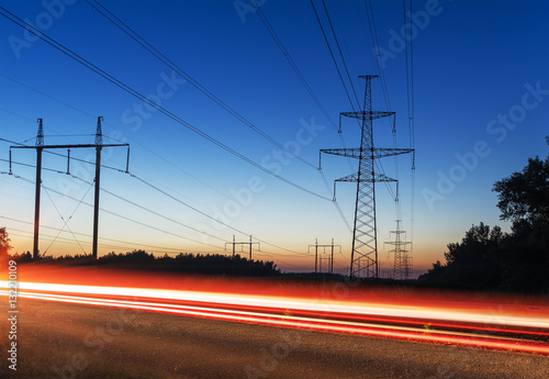 power transmission tower and lines at sunset tracks from cars.