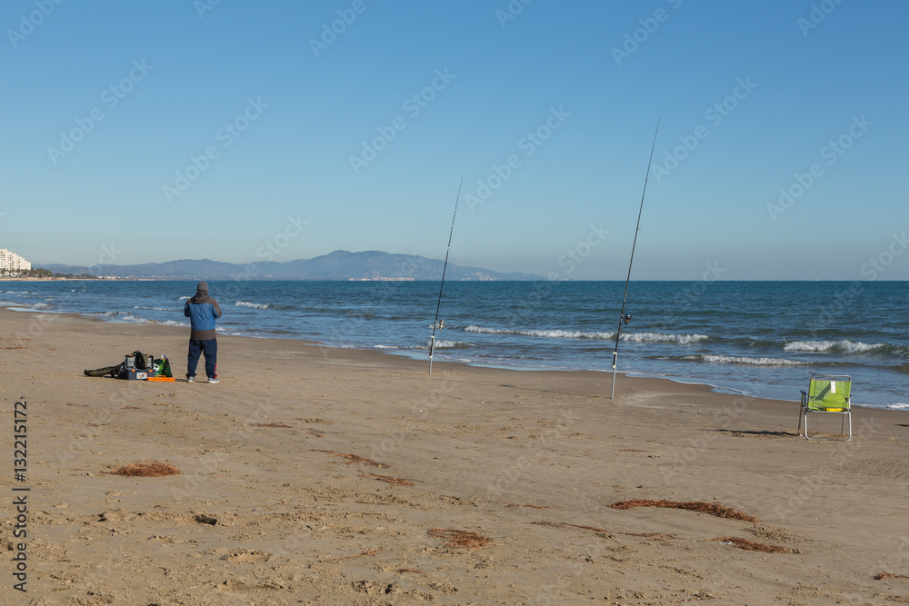 Man fiskar med kastspö på en sandstrand vid havet