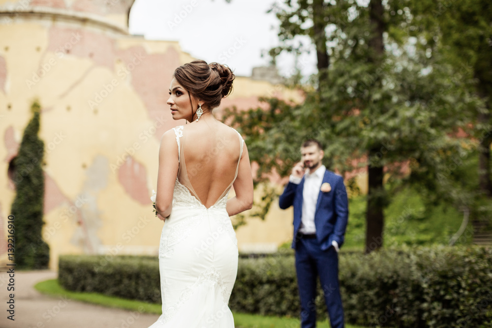 Naklejka premium portrait of a beautiful happy brunette bride in wedding white dress holding hands in bouquet of flowers outdoors on the background of green leaves