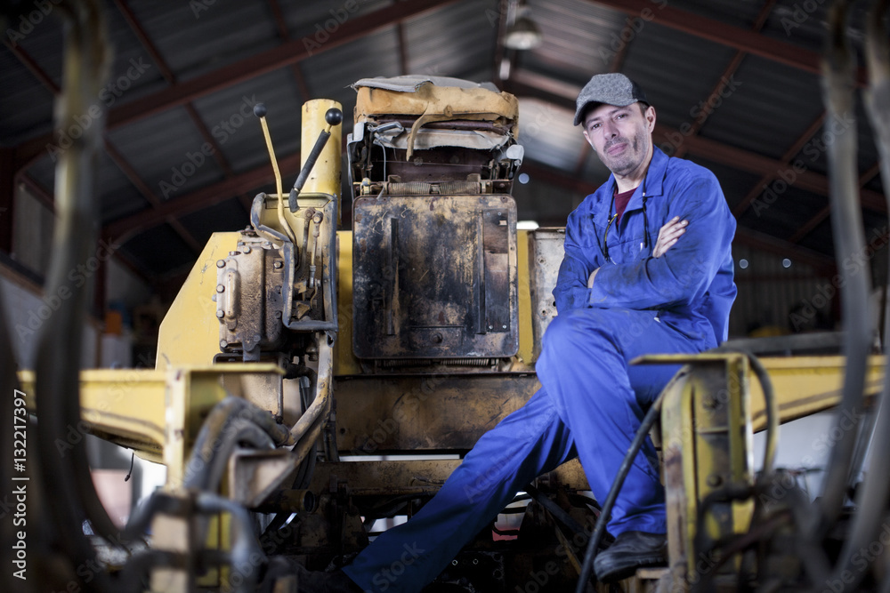 Man wearing blue overalls sitting on machine in workshop Man wearing blue overalls sitting on machine in workshop