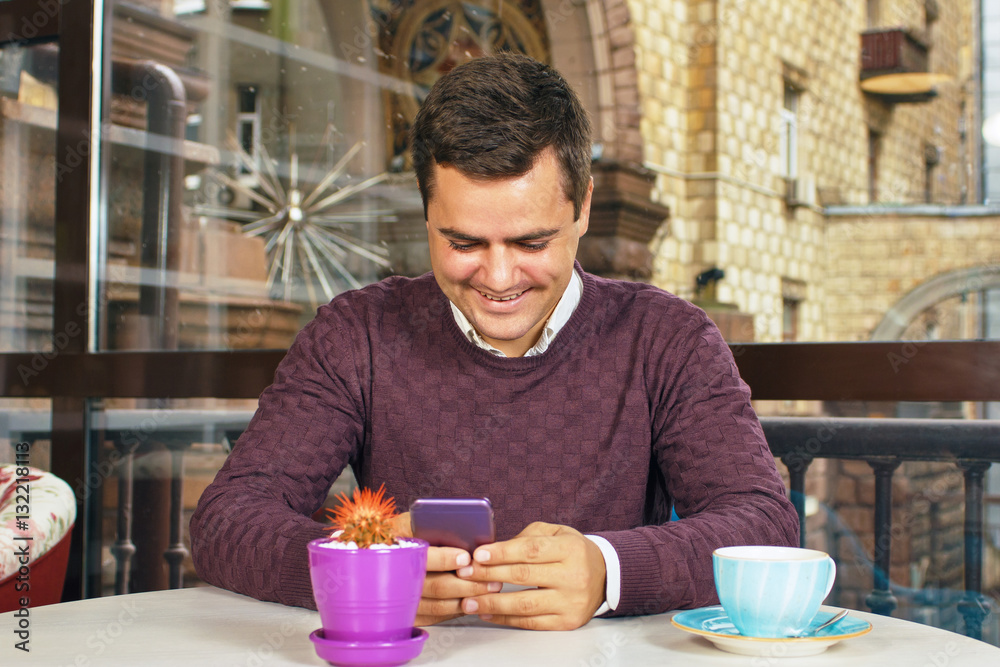 Young man holding a mobile phone and smiling. Read the posts and drinking coffee. Young man holding a mobile phone and smiling. Read the posts and drinking coffee.