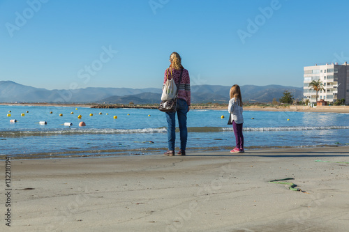 Kvinna och barn tittar ut över en strand med bojar till fiskenät photo