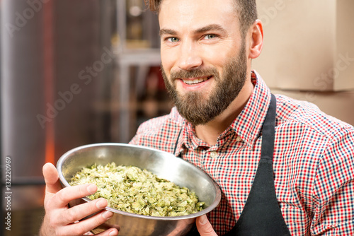 Portrait of a brewer with green hops dressed in apron and checkered shirt at the manufacturing