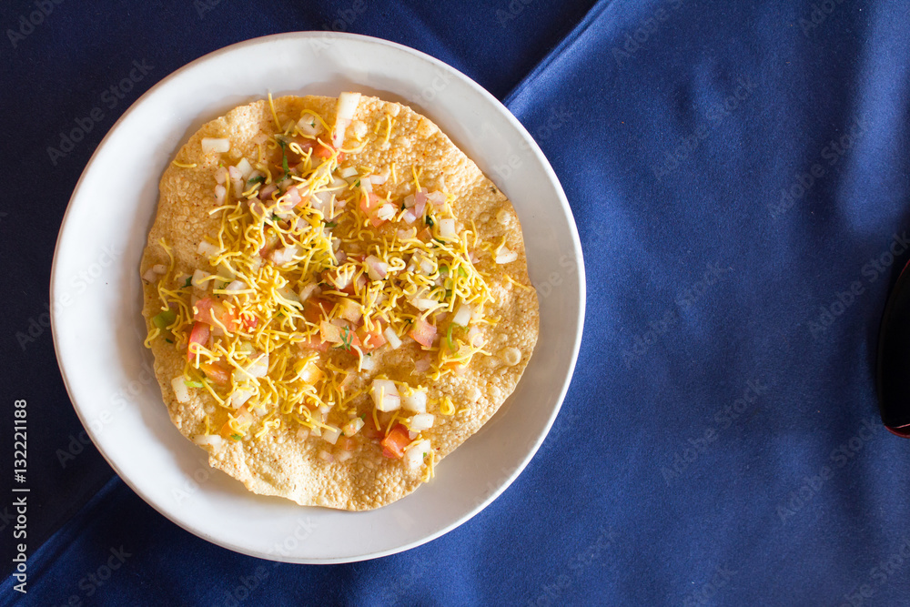 Indian food (Masala papad) on white dish with blue background Indian food (Masala papad) on white dish with blue background