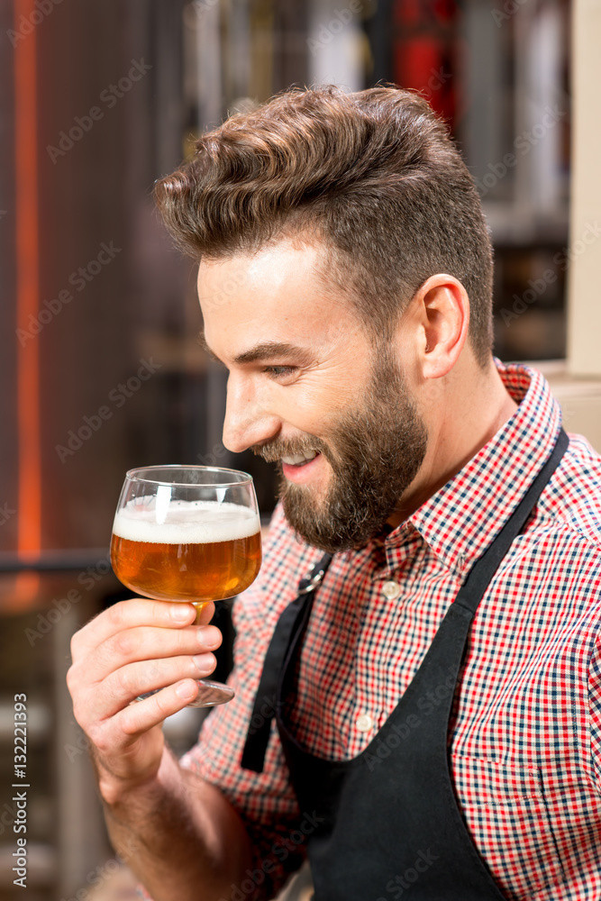 Handsome brewer expertising beer in the glass at the manufacturing