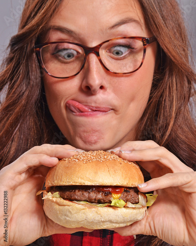 Graciosa y expresiva mujer nerd comiendo hamburguesa.