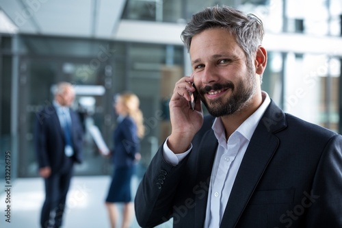 Smiling businessman talking on mobile phone in office corridor