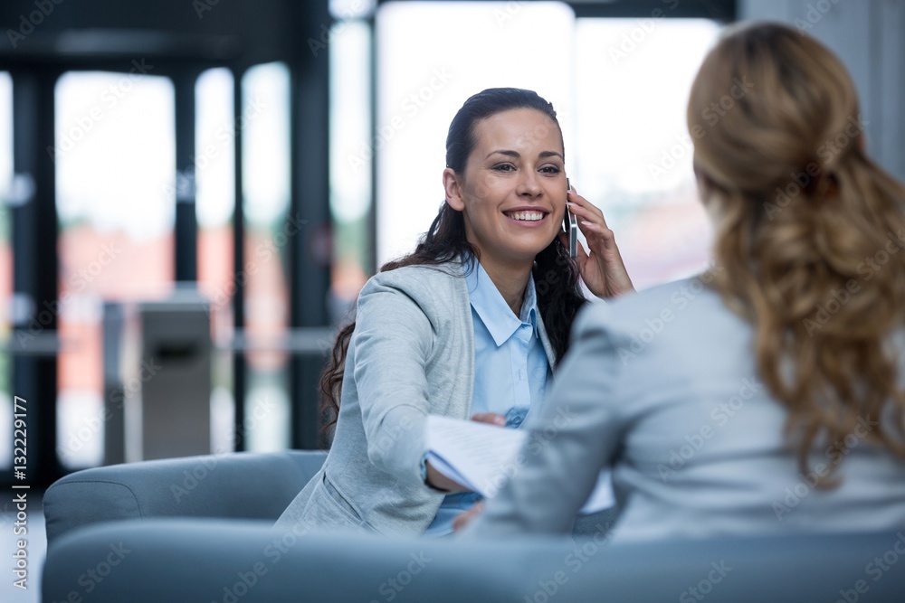 Obraz premium Businesswoman sitting with colleague and talking on mobile phone