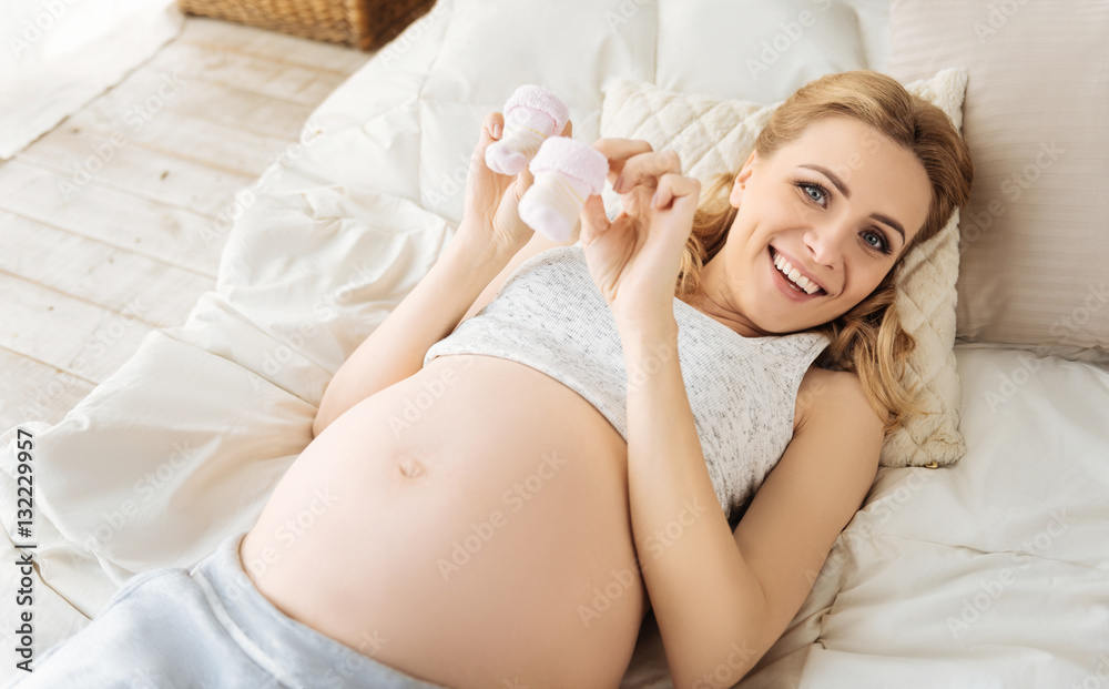 Pregnant woman demonstrating baby socks in bed Pregnant woman demonstrating baby socks in bed