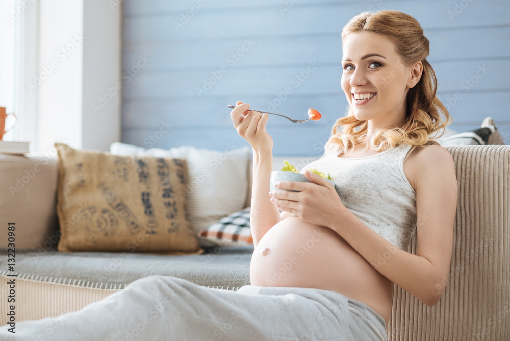 Pregnant woman eating salad on the sofa Pregnant woman eating salad on the sofa