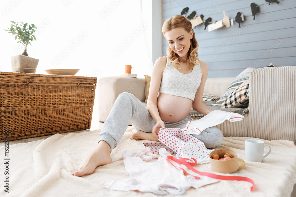 Pregnant young woman smiling happily at new baby clothes