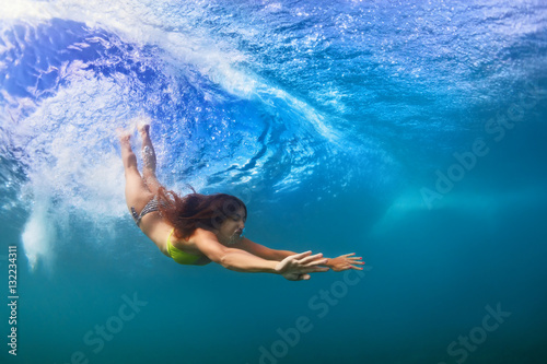 Young sportive girl in bikini in action. Fit woman swim underwater, dive under breaking ocean wave. Healthy lifestyle. Water sports, extreme surfing in outdoor adventure camp on summer beach vacation